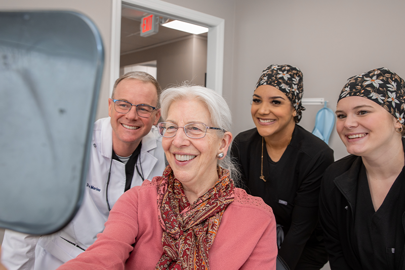 Dr. Marino, staff and patient smiling with mirror